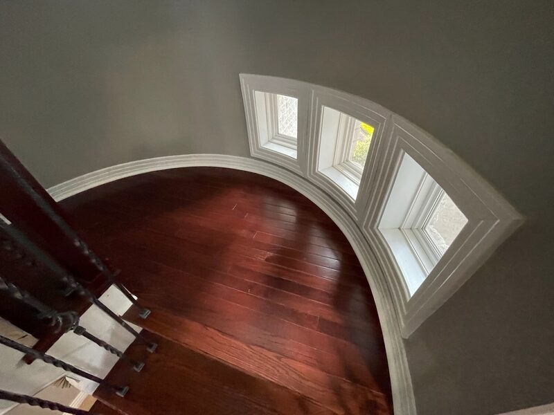 Stained hardwood floor on a curved upper landing beside a staircase